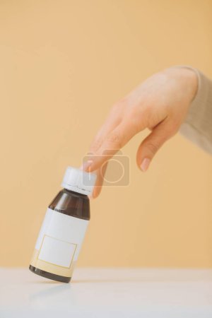Foto de Una mano femenina toca una botella de pastillas sobre un fondo beige. - Imagen libre de derechos