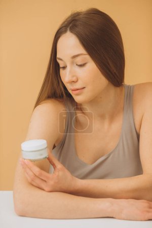 Foto de Retrato de moda de una hermosa mujer con una botella de crema cosmética sobre un fondo beige pastel. - Imagen libre de derechos