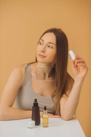 Téléchargez les photos : Belle femme avec des bouteilles de cosmétiques posant sur un fond beige. - en image libre de droit