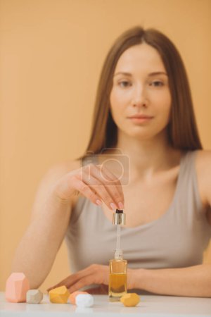 Photo for A beautiful girl poses with face serum or hair oil on a beige background. - Royalty Free Image