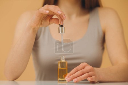Téléchargez les photos : Portrait de beauté d'une femme tenant une bouteille compte-gouttes isolée sur fond beige. - en image libre de droit