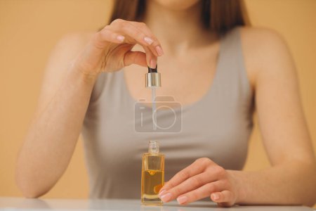 Téléchargez les photos : Portrait de beauté d'une femme tenant une bouteille compte-gouttes isolée sur fond beige. - en image libre de droit