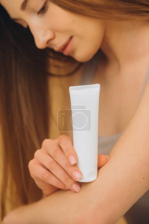 Téléchargez les photos : Une femme tient un tube avec une crème cosmétique. Portrait studio d'une jolie femme sur fond beige. Gros plan. - en image libre de droit