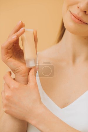 Téléchargez les photos : Une femme tient un tube avec une crème cosmétique. Portrait studio d'une jolie femme sur fond beige. Gros plan. - en image libre de droit