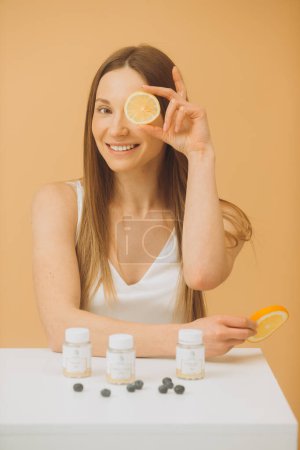Photo for Beautiful girl with a fresh orange and bottles of vitamins on a beige background. - Royalty Free Image