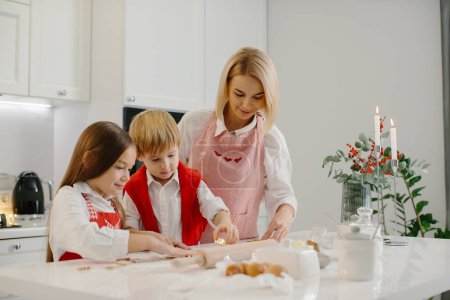 Foto de Madre feliz con los niños cortando diferentes formas de galletas en la cocina. Madre con hija e hijo están haciendo galletas de Navidad en casa y divertirse. - Imagen libre de derechos