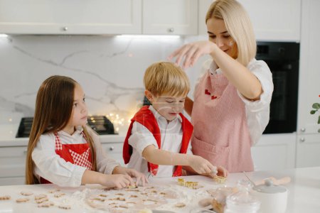 Téléchargez les photos : Les enfants et leur mère ont découpé les biscuits de la pâte. Une petite fille et un garçon font des biscuits de Noël dans la cuisine. - en image libre de droit