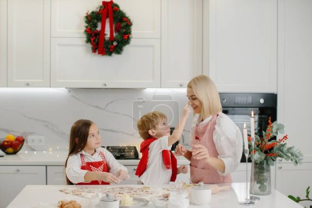 Foto de Feliz madre e hijos jugando con masa de galletas en la mesa de la cocina mientras hacen galletas de Navidad. - Imagen libre de derechos