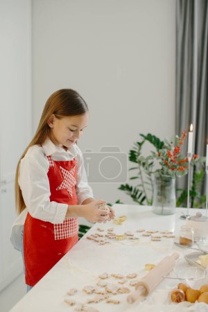 Foto de Una niña está haciendo galletas de Navidad en la cocina.. - Imagen libre de derechos
