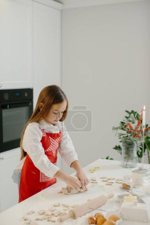 Téléchargez les photos : Une petite fille fait des biscuits de Noël dans la cuisine. - en image libre de droit