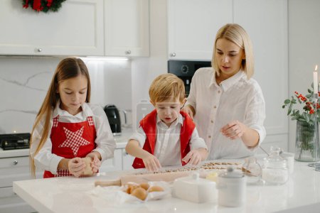 Téléchargez les photos : Une mère apprend à sa fille et son petit fils à faire des biscuits. Une femme et ses enfants préparent des biscuits de Noël à l'aide d'un moule à pâte. - en image libre de droit
