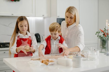 Téléchargez les photos : Une mère apprend à sa fille et son petit fils à faire des biscuits. Une femme et ses enfants préparent des biscuits de Noël à l'aide d'un moule à pâte. - en image libre de droit