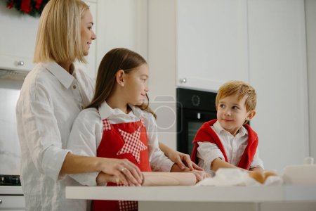 Téléchargez les photos : Noël, la mère et les enfants font des biscuits dans la cuisine. Mère apprend aux enfants à faire des biscuits. - en image libre de droit