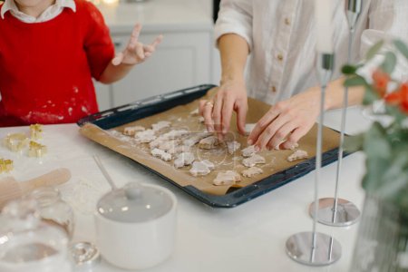 Téléchargez les photos : Une mère avec sa fille et son fils prépare des biscuits de Noël, les enfants mettent des biscuits sur une plaque à pâtisserie. Gros plan. - en image libre de droit