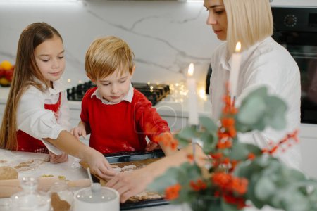 Photo for A mother with her daughter and son prepares Christmas cookies, children put cookies on a baking sheet. - Royalty Free Image