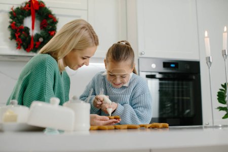 Photo for Mother and daughter decorate Christmas cookies in the kitchen. - Royalty Free Image
