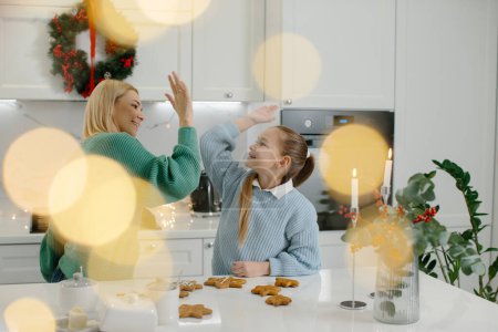 Photo for A cute little girl and her beautiful mother give high fives and smile while making Christmas cookies at home. - Royalty Free Image