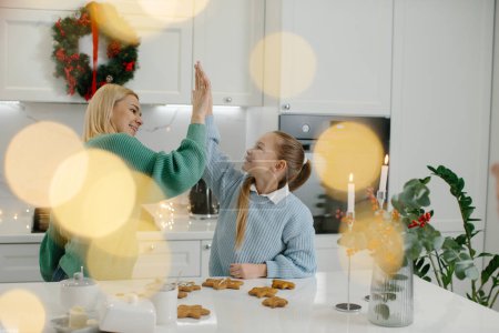 Téléchargez les photos : Une petite fille mignonne et sa belle mère donnent cinq hauts et sourire tout en faisant des biscuits de Noël à la maison. - en image libre de droit