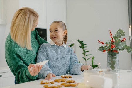 Téléchargez les photos : Jeune mère heureuse étreint sa petite fille dans la cuisine tout en faisant des biscuits au pain d'épice. - en image libre de droit