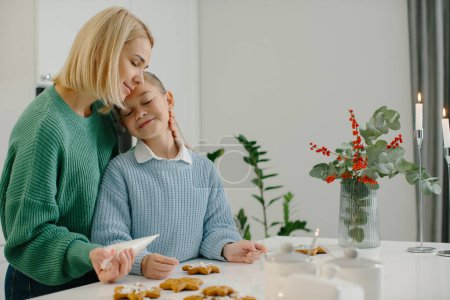 Téléchargez les photos : Jeune mère heureuse étreint sa petite fille dans la cuisine tout en faisant des biscuits au pain d'épice. - en image libre de droit