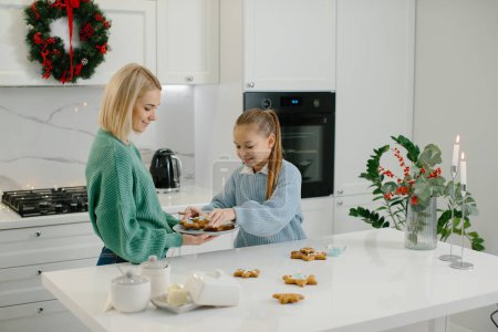 Foto de Madre e hija decoran galletas de Navidad en la cocina. - Imagen libre de derechos