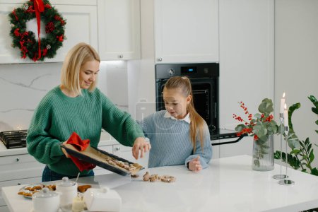 Photo for Mother and daughter are putting freshly baked cookies on the table. - Royalty Free Image
