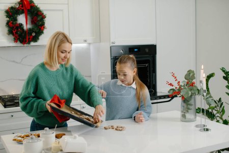 Téléchargez les photos : Mère et fille mettent des biscuits fraîchement cuits sur la table. - en image libre de droit