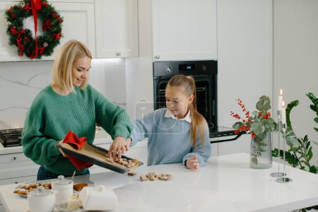 Foto de Madre e hija están poniendo galletas recién horneadas en la mesa. - Imagen libre de derechos