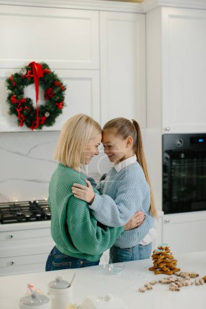 Foto de Feliz madre e hija se abrazan en la cocina después de terminar de hornear galletas de Navidad. - Imagen libre de derechos