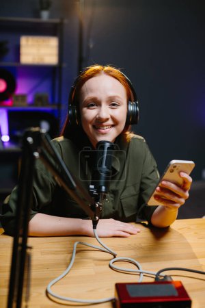 Photo for The girl in headphones speaks into the microphone while holding the phone in her hands. The concept of online broadcasts. - Royalty Free Image