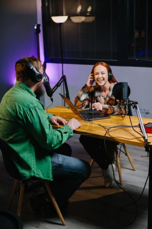 A podcast host and a guest have fun chatting during a live online broadcast in a home studio.