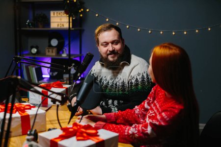 Foto de Un par de bloggers están haciendo un regalo de Navidad en su canal. Presentadores de radio en suéteres de Navidad llevan a cabo una rifa de regalos entre los oyentes. - Imagen libre de derechos