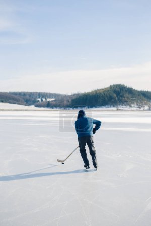 Photo for Senior man playing hockey on a frozen lake in winter. - Royalty Free Image