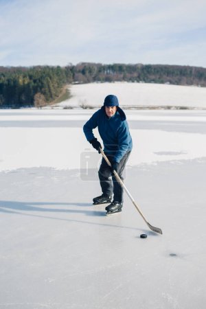 Téléchargez les photos : Homme âgé jouant au hockey sur un lac gelé en hiver. - en image libre de droit