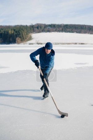 Foto de Hombre mayor en patines de hielo con palo de hockey en el lago congelado en invierno. Concepto Hobby de las personas mayores. - Imagen libre de derechos