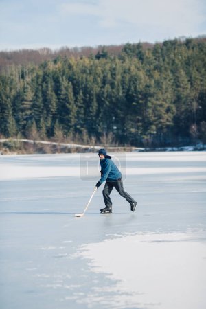 Foto de Un anciano practica hockey sobre hielo en un lago congelado en invierno. - Imagen libre de derechos