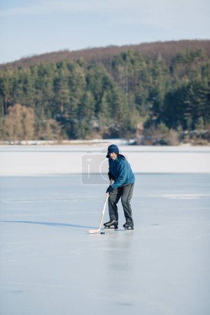 Téléchargez les photos : Un homme âgé pratique le hockey sur glace sur un lac gelé en hiver. - en image libre de droit