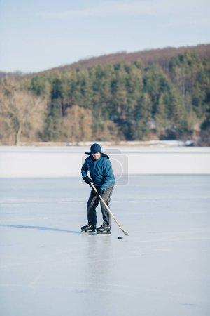 Téléchargez les photos : Un homme âgé pratique le hockey sur glace sur un lac gelé en hiver. - en image libre de droit
