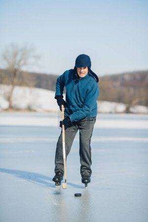 Photo for An elderly man practices ice hockey on a frozen lake in winter. - Royalty Free Image
