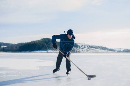 Téléchargez les photos : Un homme âgé pratique la rigueur de la rondelle avec des bâtons de hockey sur un lac gelé en hiver. - en image libre de droit