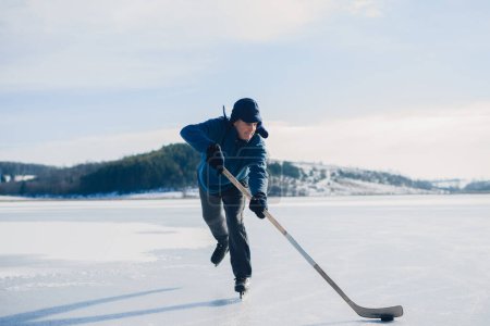 Photo for An elderly man practices stricking the puck with hockey sticks on a frozen lake in winter. - Royalty Free Image