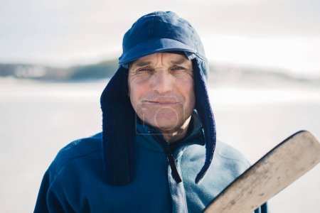 Foto de Un anciano con un palo de hockey en un lago congelado en invierno. Mirando a la cámara. - Imagen libre de derechos