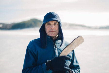 Téléchargez les photos : Homme âgé avec un bâton de hockey sur un lac gelé en hiver. Regardant dans la caméra. - en image libre de droit