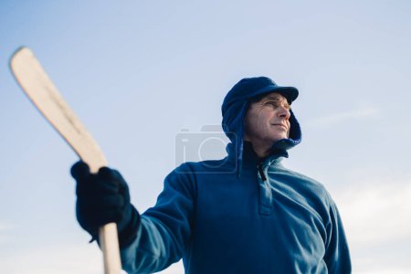Téléchargez les photos : Portrait d'un homme âgé avec un bâton de hockey sur fond de ciel. - en image libre de droit