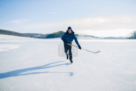 Foto de Hombre mayor en patines de hielo con palo de hockey en el lago congelado en invierno. Concepto Hobby de las personas mayores. - Imagen libre de derechos