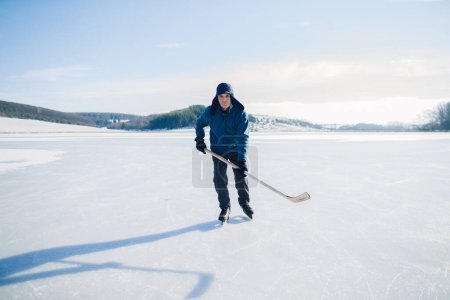 Téléchargez les photos : Homme âgé avec bâton de hockey patinant sur glace en hiver. Regardant dans la caméra. - en image libre de droit