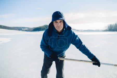 Foto de Hombre mayor con palo de hockey patinando sobre hielo en invierno. Mirando a la cámara. - Imagen libre de derechos