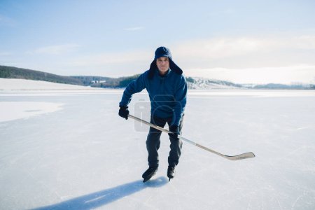 Foto de Hombre mayor con palo de hockey patinando sobre hielo en invierno. Mirando a la cámara. - Imagen libre de derechos