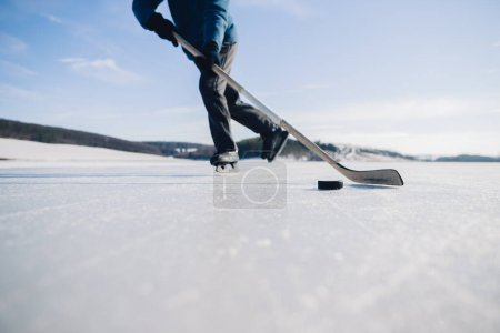 Photo for An elderly man practices stricking the puck with hockey stick on a frozen lake in winter. - Royalty Free Image