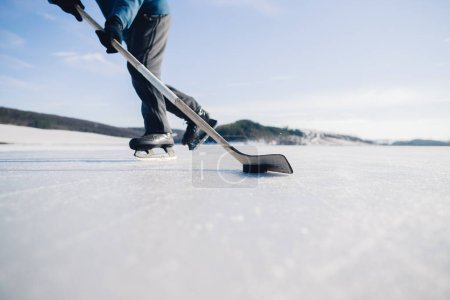 Foto de Un anciano practica el stricking del disco con palo de hockey en un lago congelado en invierno. - Imagen libre de derechos